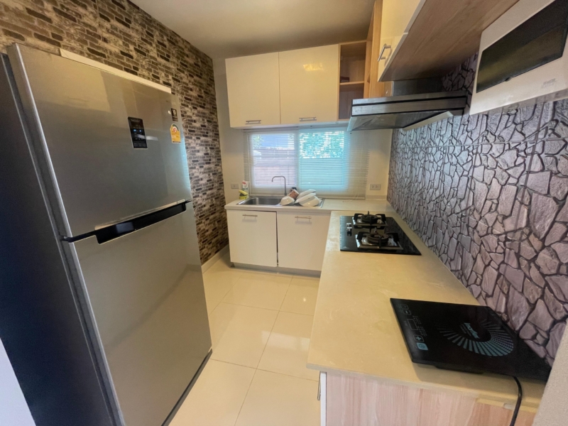 Modern kitchen with stainless steel refrigerator, white cabinets, sink, and decorative brick and stone walls.