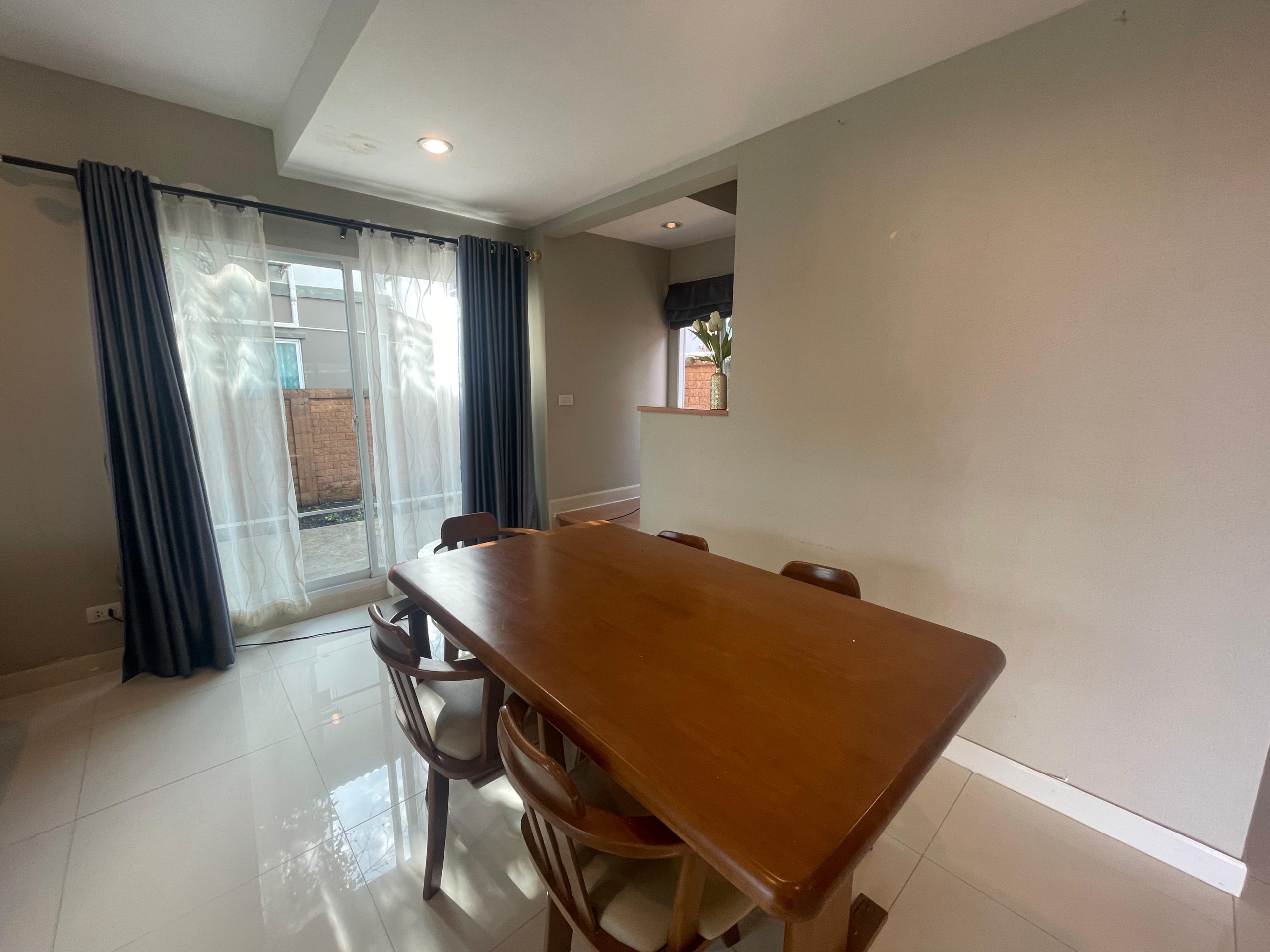 Spacious dining room with wooden table, chairs, tiled floor, and glass doors leading to a garden.